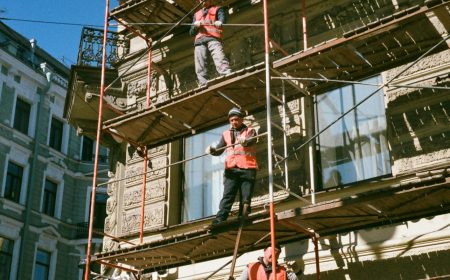 Construction workers on scaffolding renovating a building facade on a sunny day.